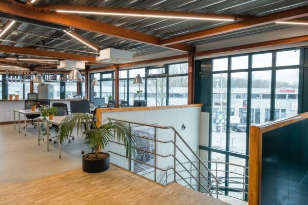 Modern ingericht kantoor met veel daglicht aan de Johan van Hasseltweg, met werkplekken, planten en een bar in industriële stijl.